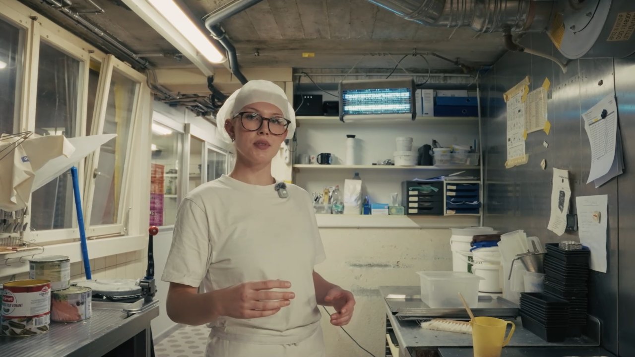 Standbild aus dem Film: eine junge Köchin mit Haube und Ansteckmikrofon spricht in einer Grossküche in die Kamera.